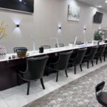 Row of nail salon workstations with black chairs and manicure supplies on a counter.